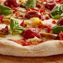 Zbliżenie na pizzę z pomidorkami koktajlowymi, mozzarellą, bazylią i suszonymi pomidorami.