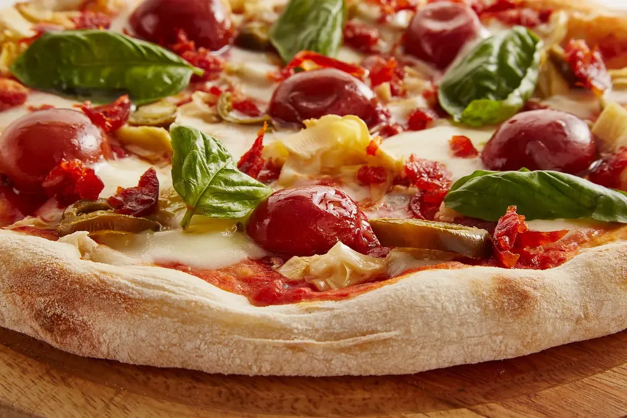 Zbliżenie na pizzę z pomidorkami koktajlowymi, mozzarellą, bazylią i suszonymi pomidorami.